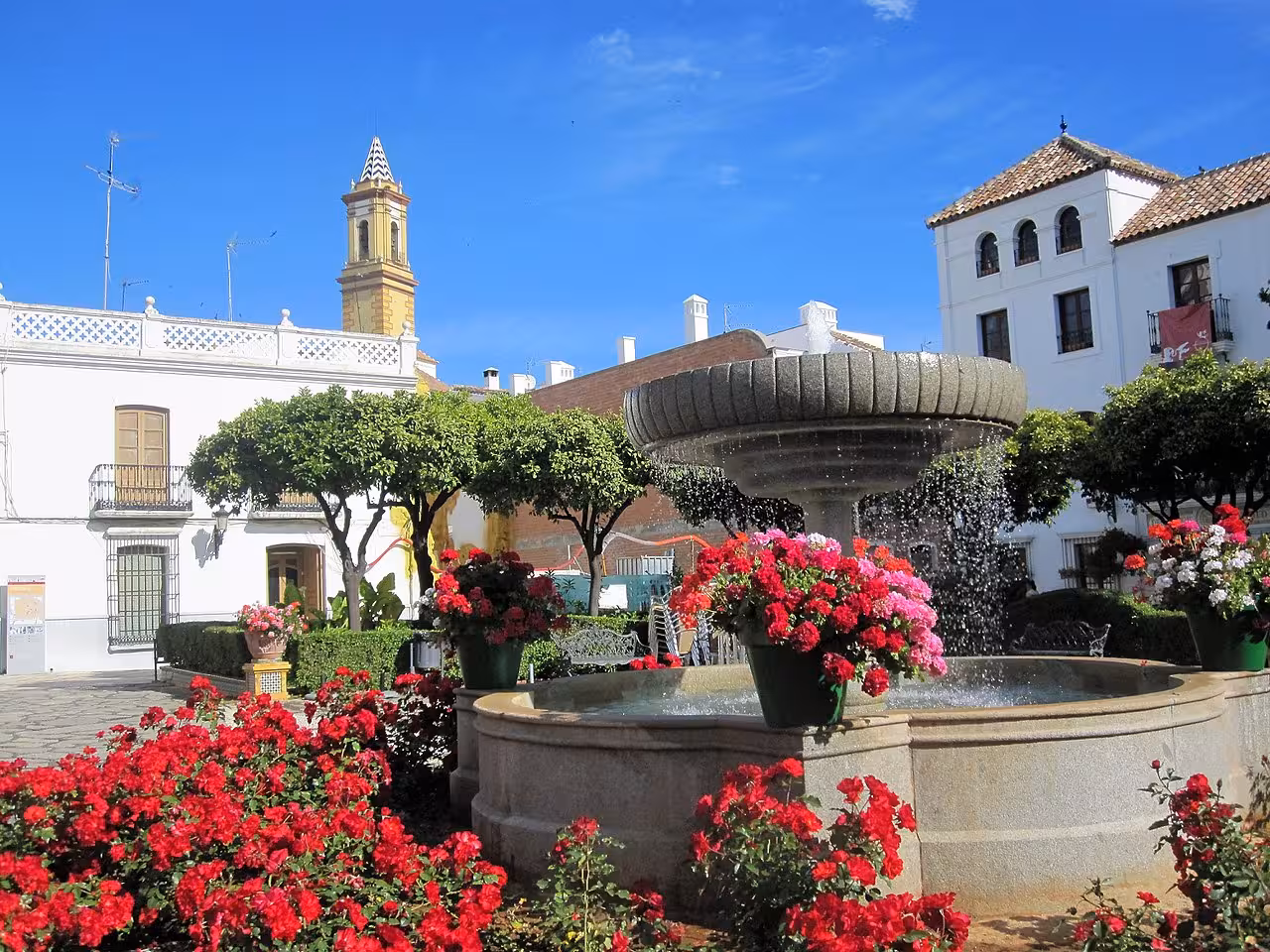 Charming Estepona plaza with vibrant flowers, a central fountain, and historic architecture under a clear blue sky.