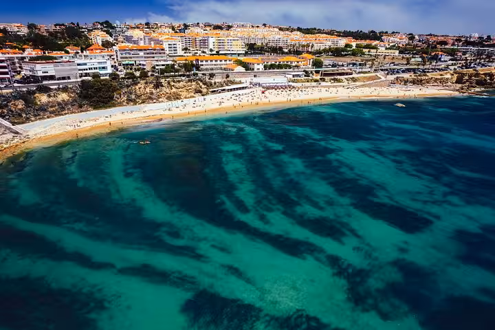 Aerial view of Estoril beach with turquoise waters and bustling shoreline, perfect for a Lisbon beach and wine tour.