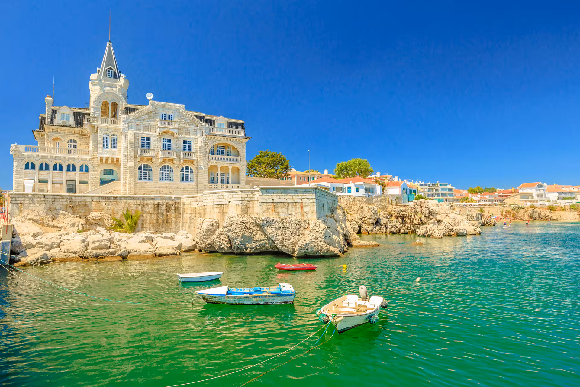 Historic seaside mansion overlooking vibrant green waters with moored boats in Estoril, Portugal.