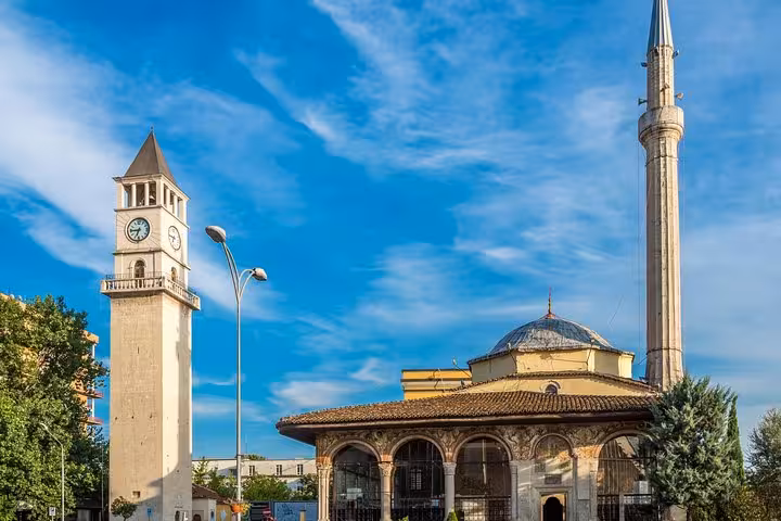 Iconic Et'hem Bey Mosque and Clock Tower under a vibrant blue sky in Tirana, a highlight of the Albania tour.