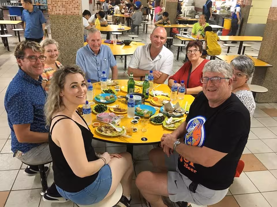 Group of tourists enjoying a vibrant meal at a bustling hawker center during a UNESCO street food tour.