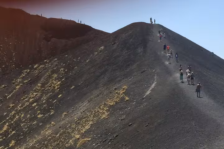 Group of trekkers ascend the steep black volcanic path of Mount Etna, capturing the adventurous spirit of Sicily tours.