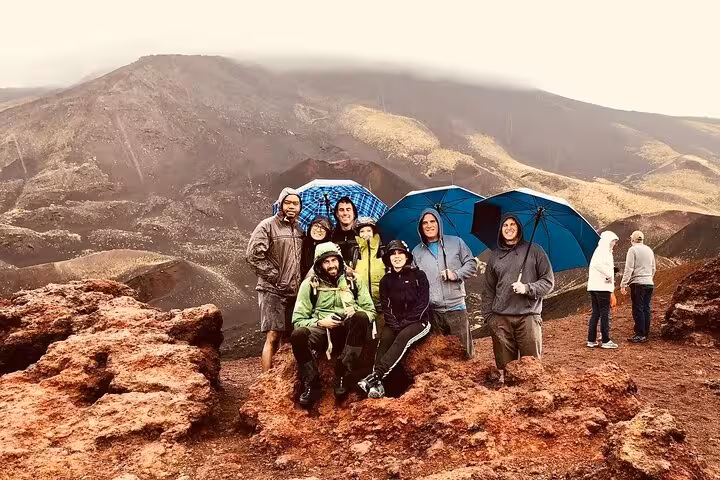 Group of tourists with umbrellas enjoying scenic views on Mount Etna, highlighting adventure and camaraderie.