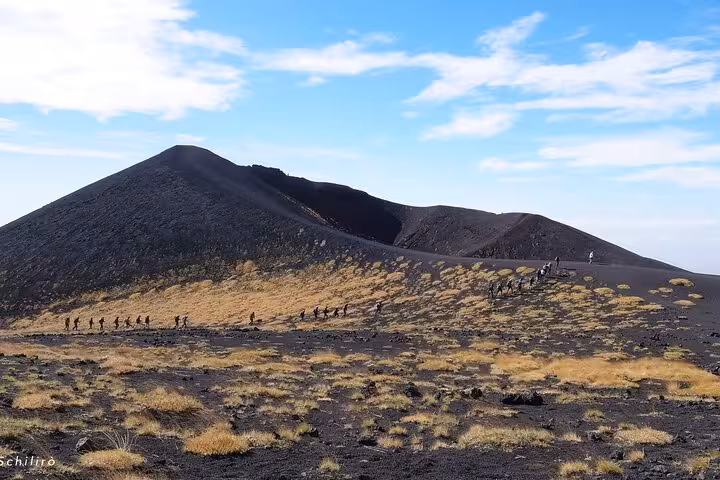 Hikers trek along the rugged slopes of Mount Etna under a clear blue sky, showcasing Sicily's volcanic landscape.