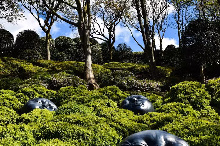 Dark bronze sculptures emerging from lush green hedges in a French garden with tall trees