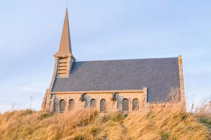 Historic stone chapel with pointed spire on grassy hill in Etretat, Normandy France