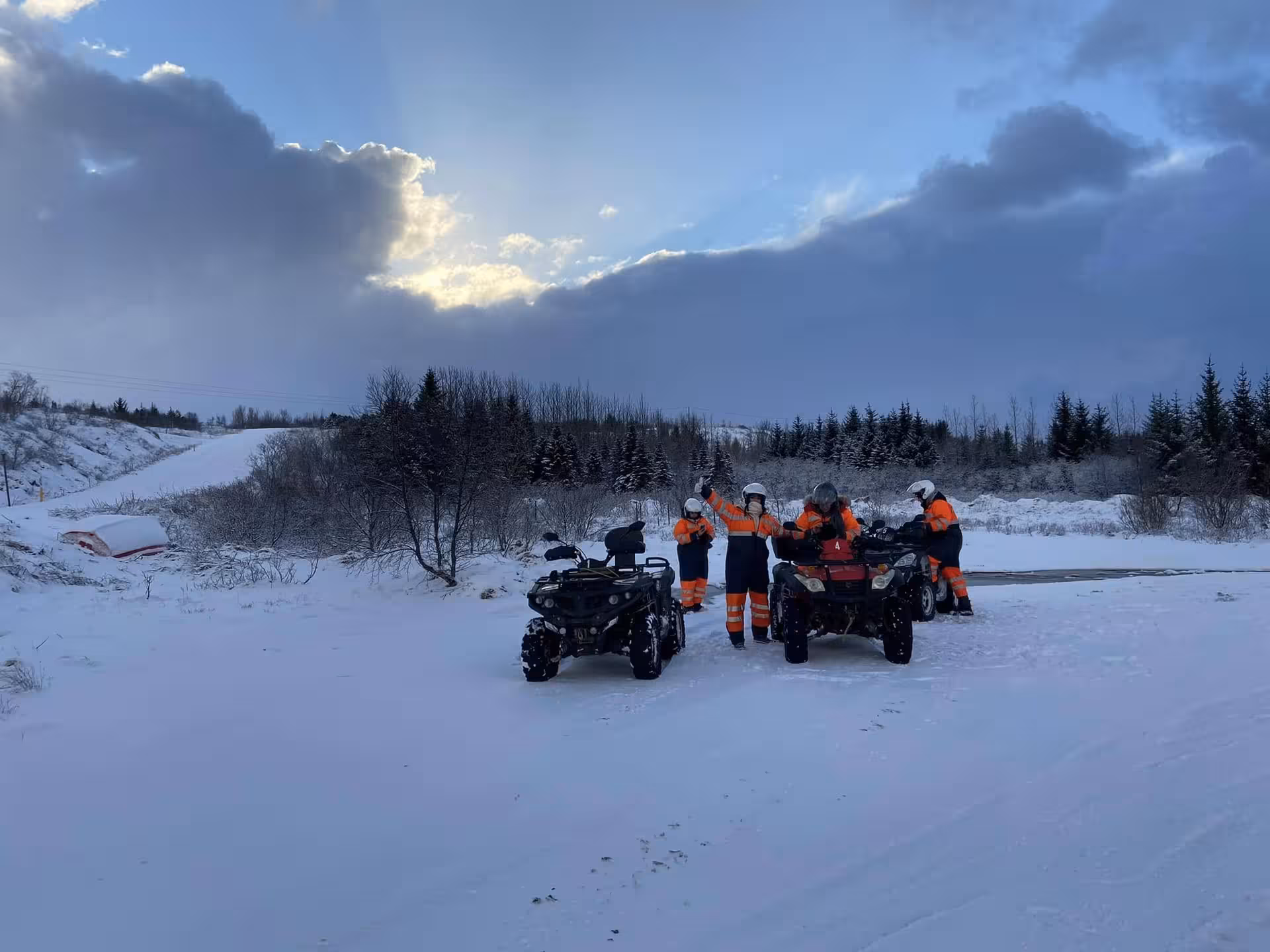 Group in orange suits riding ATV quad bikes on snowy wilderness trail near Reykjavik at sunset