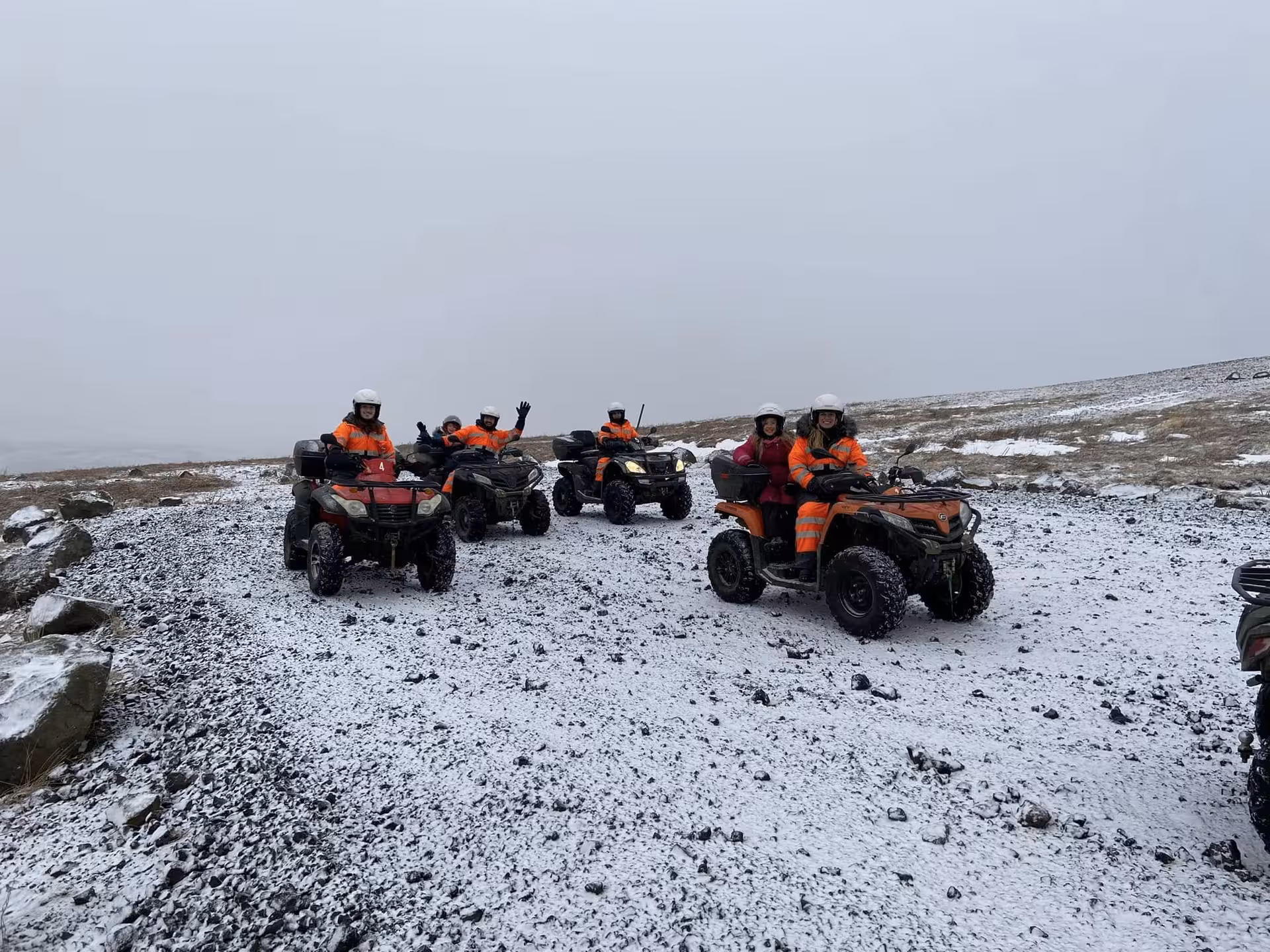 Group of riders on ATVs wearing orange safety gear on a snowy volcanic landscape in Reykjavik wilderness
