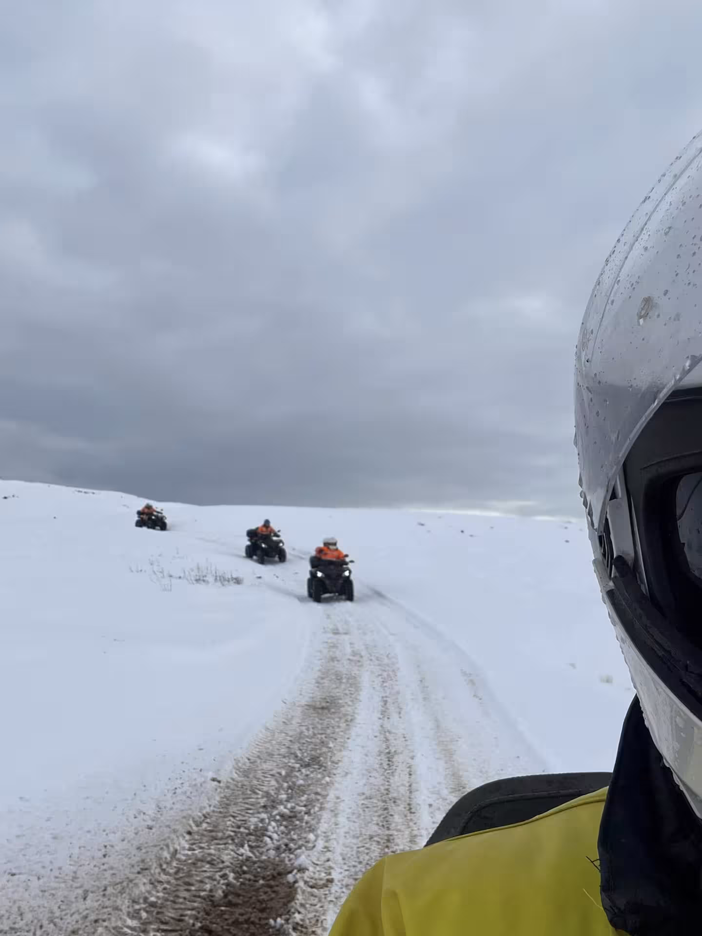 Group of riders on ATV quad bikes following a snowy trail through Iceland's winter wilderness under cloudy skies