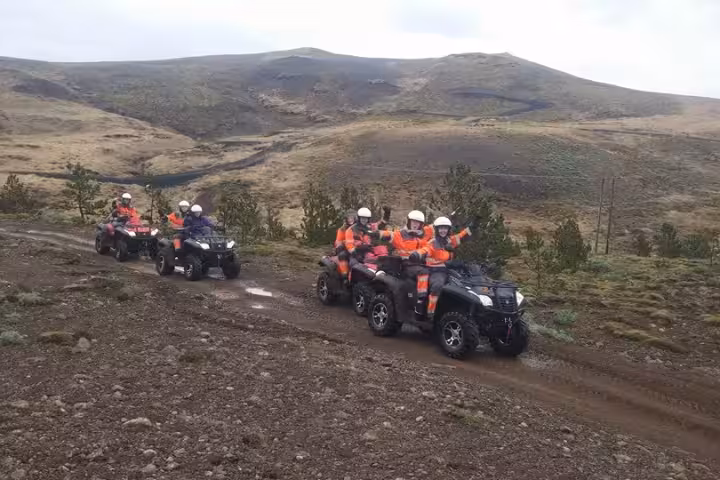 Group of riders in orange safety gear on ATV quad bikes on a dirt trail in Icelandic wilderness