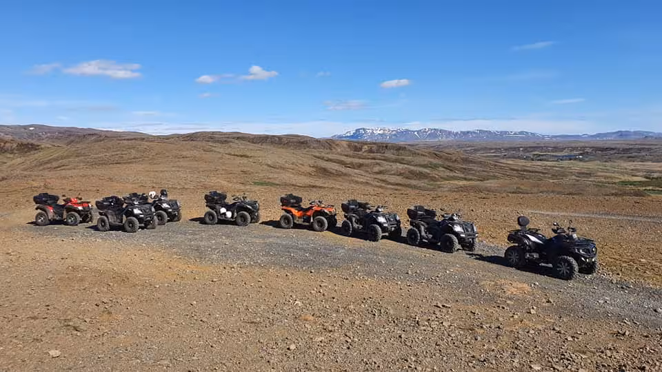 Group of ATV quad bikes parked on rocky terrain with snow-capped mountains and blue sky in Reykjavik wilderness