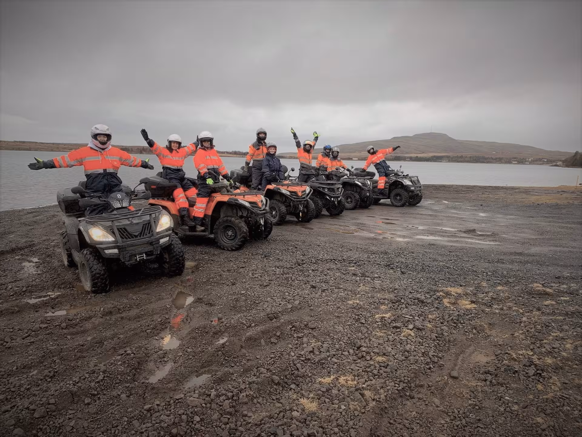 Group of riders in orange safety gear posing on ATVs near a lake in Reykjavik wilderness