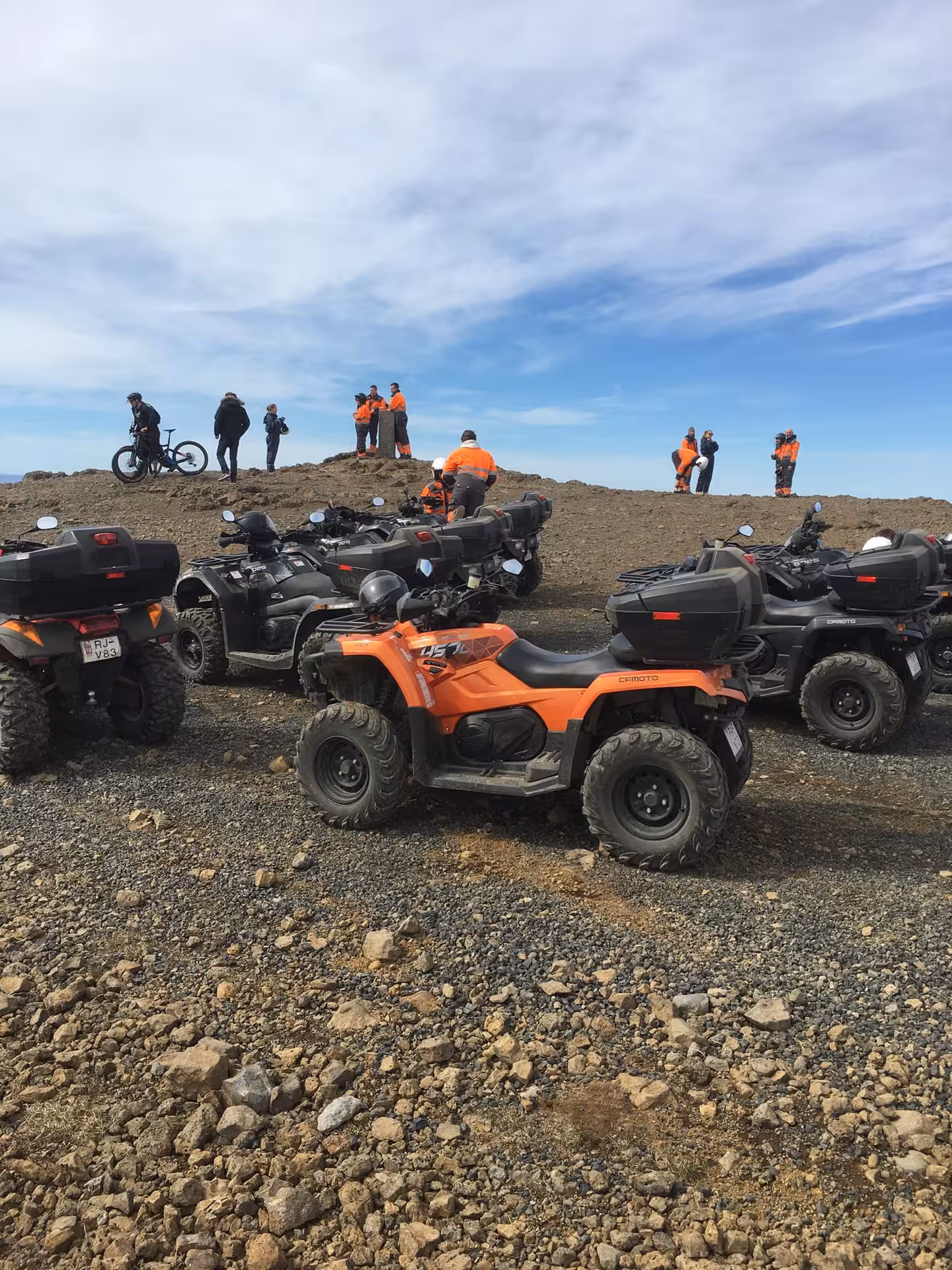 Orange and black CFMOTO ATVs parked on rocky volcanic terrain with riders in orange suits at sunset in Reykjavik wilderness