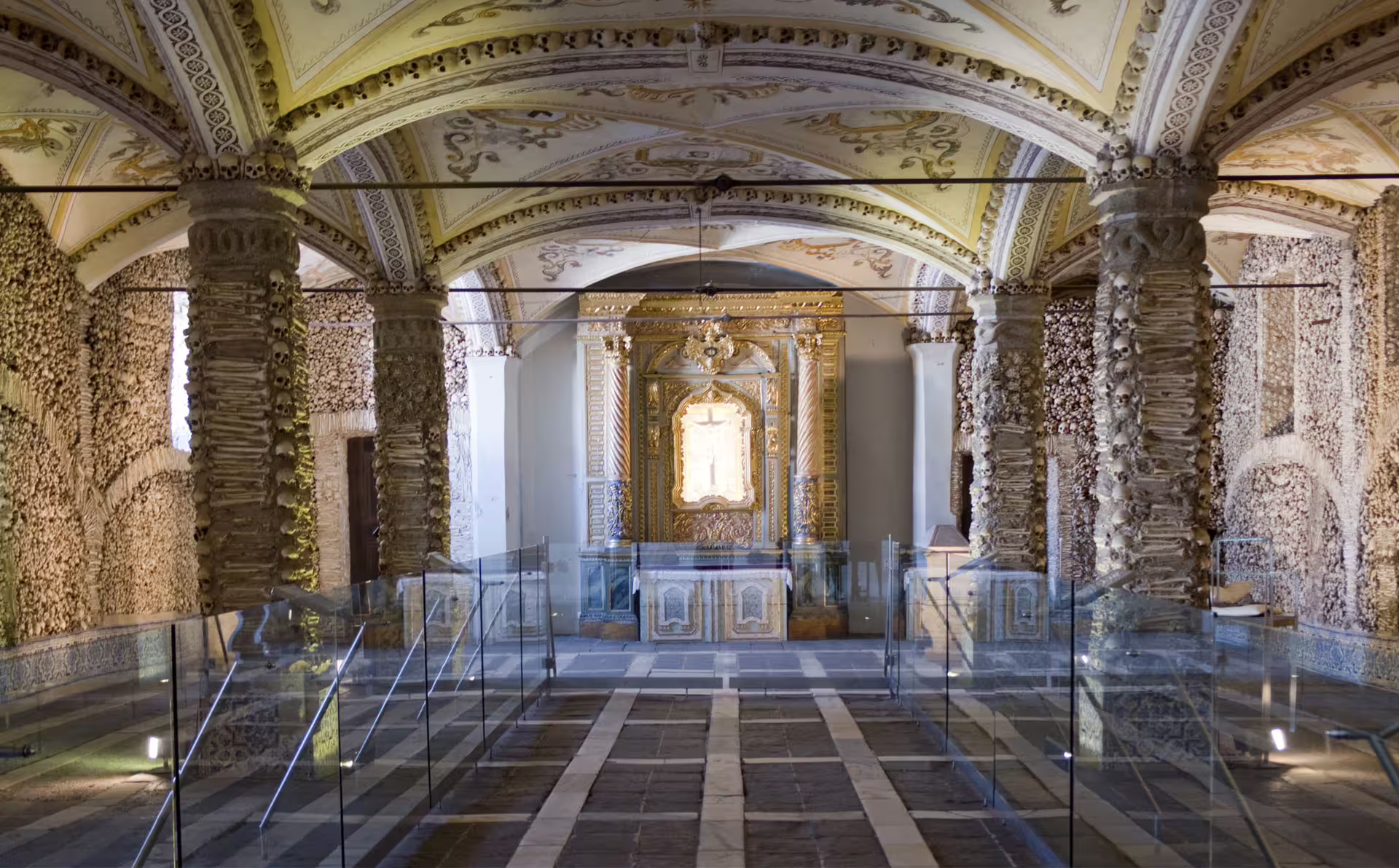 Intricate interior of Évora's Bones Chapel showcasing columns adorned with skulls and ornate golden altar.