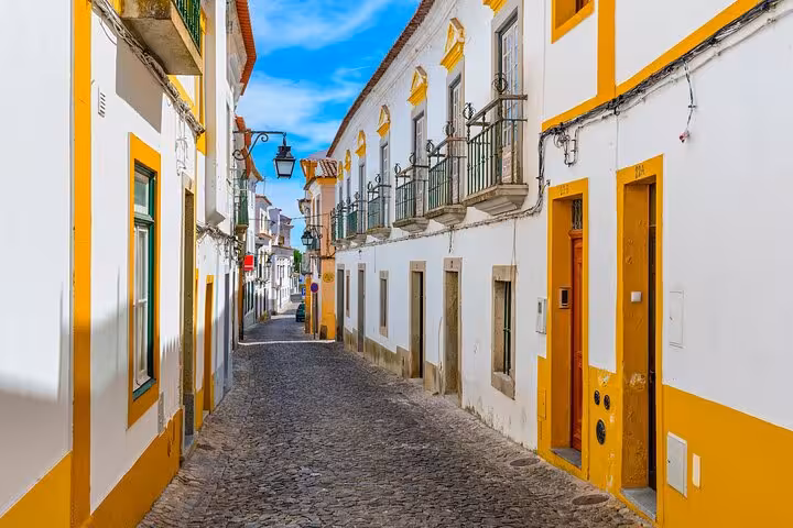 Sunny cobblestone street in Évora with traditional white and yellow buildings on a private tour.