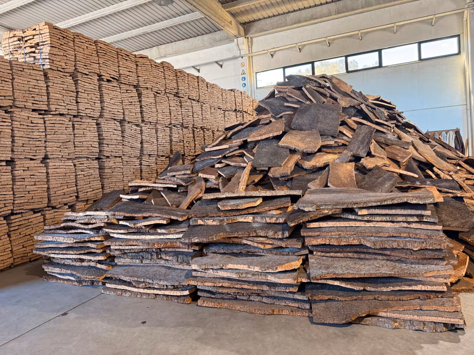 Discover traditional cork production in Évora with stacks of cork bark in a sunlit warehouse setting.