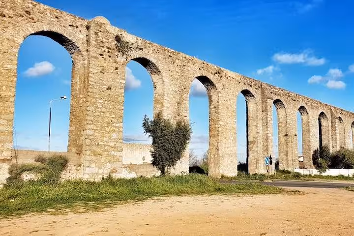 Historic aqueduct in Évora with ancient stone arches against a bright blue sky, surrounded by greenery.