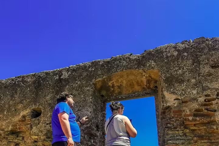 Tourists explore ancient ruins under a vibrant blue sky during a day trip from Lisbon to Évora and Monsaraz.
