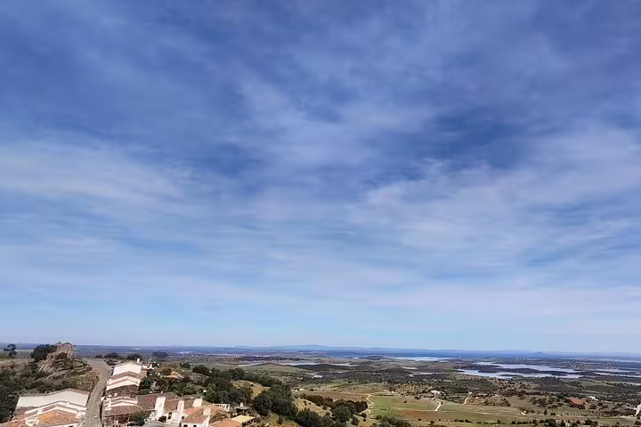 Scenic panoramic view of the Alentejo countryside from Monsaraz, showcasing rolling hills, rooftops, and expansive blue skies.
