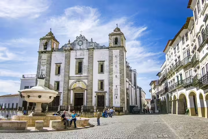 Tourists explore the picturesque Praça do Giraldo in Évora, featuring the stunning Igreja de Santo Antão and iconic fountain.