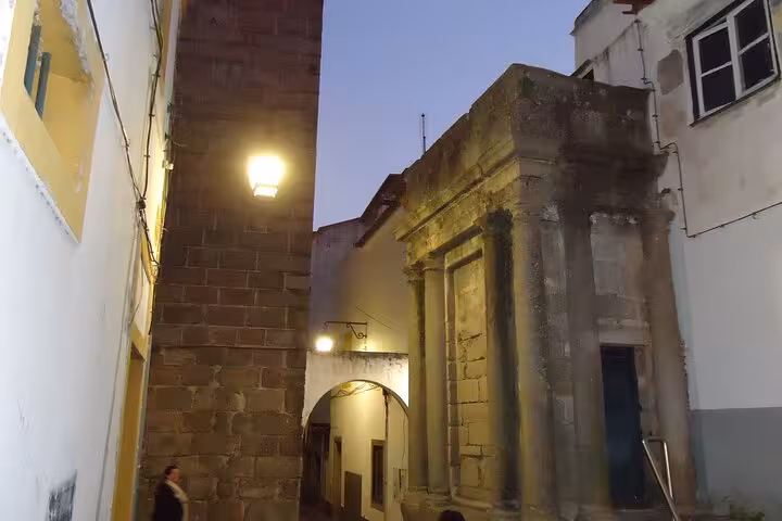Charming alleyway leading to Roman ruins in Évora, beautifully illuminated during a private evening walking tour.