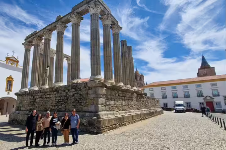 Visitors explore the ancient Roman Temple of Évora on a sunny day, a highlight of the day trip from Lisbon to Évora and Monsaraz.