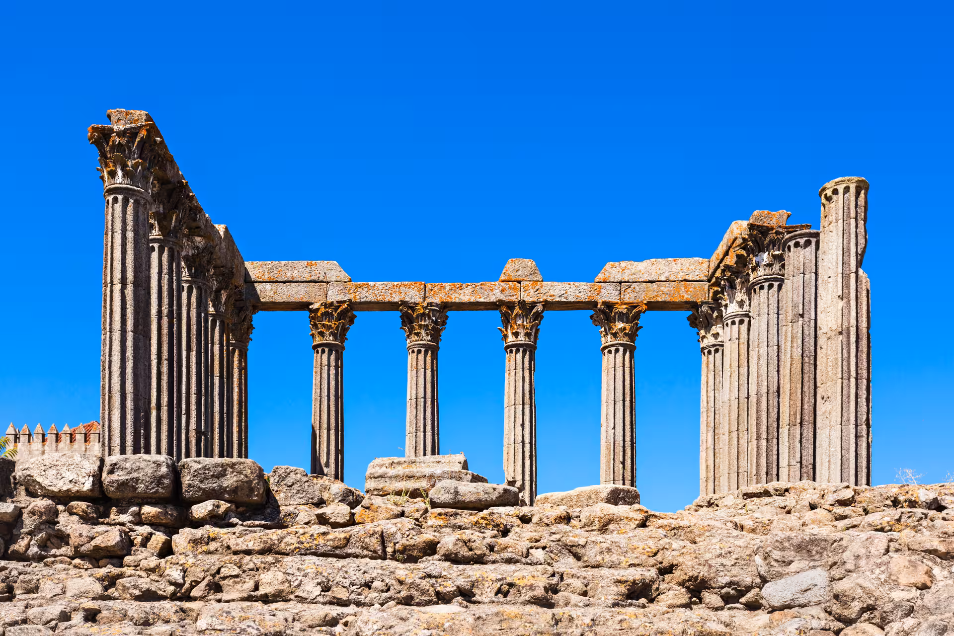 Ancient Roman temple ruins with tall stone columns stand against a clear blue sky in Évora, Portugal.