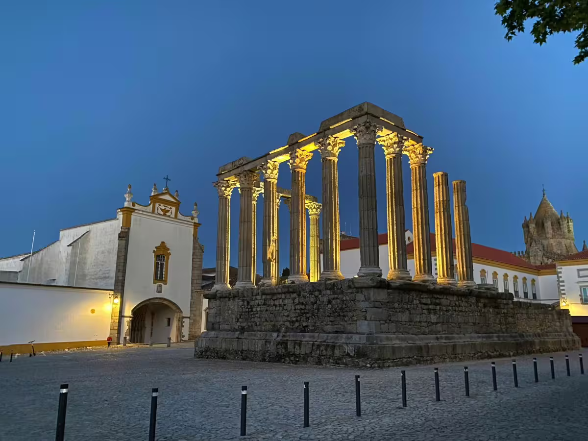 Illuminated Roman temple and church in Évora at dusk, showcasing historic architecture on Lisbon tour.