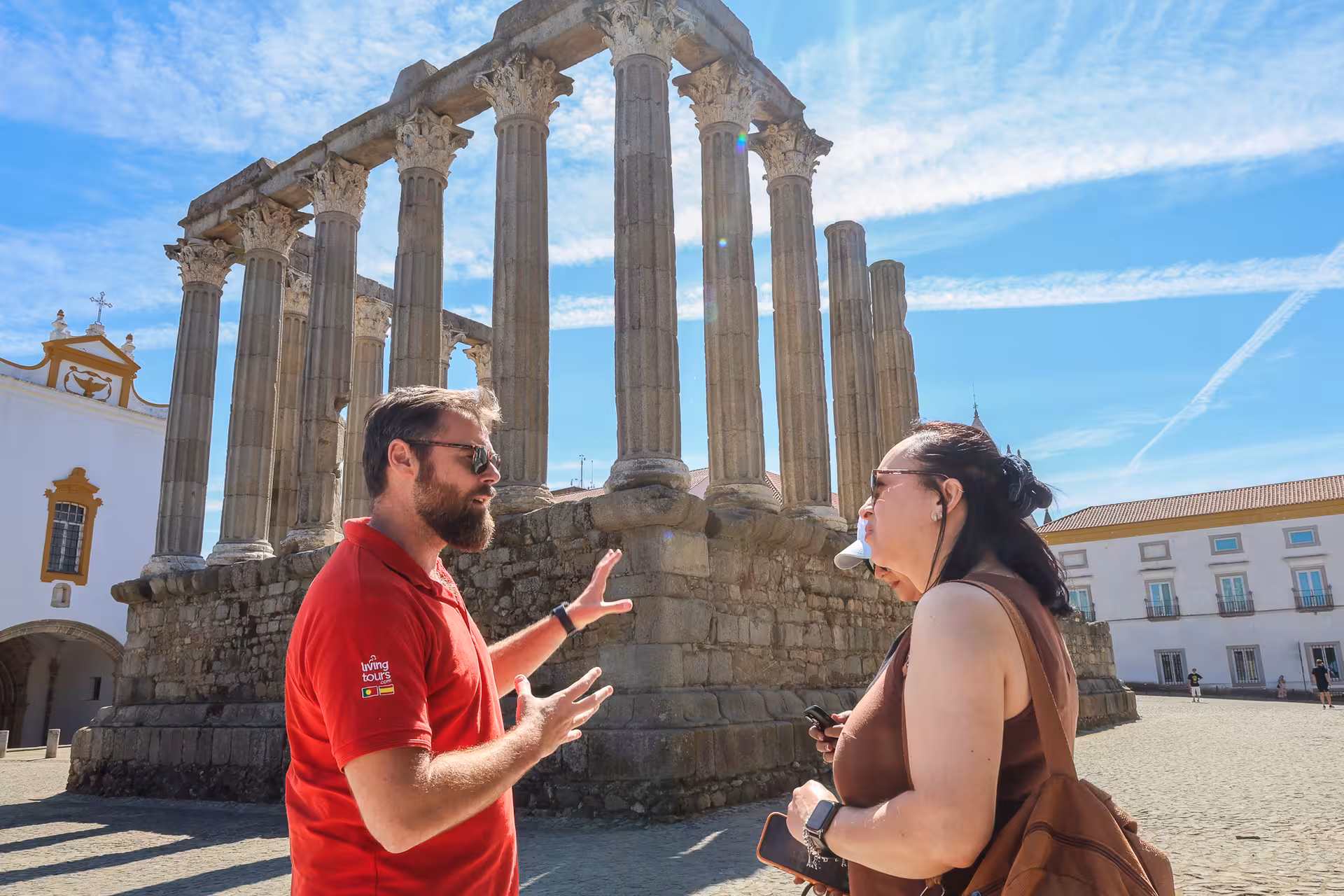 Guide explains the historical Roman Temple of Évora to a tourist under a clear blue sky on the small-group tour.