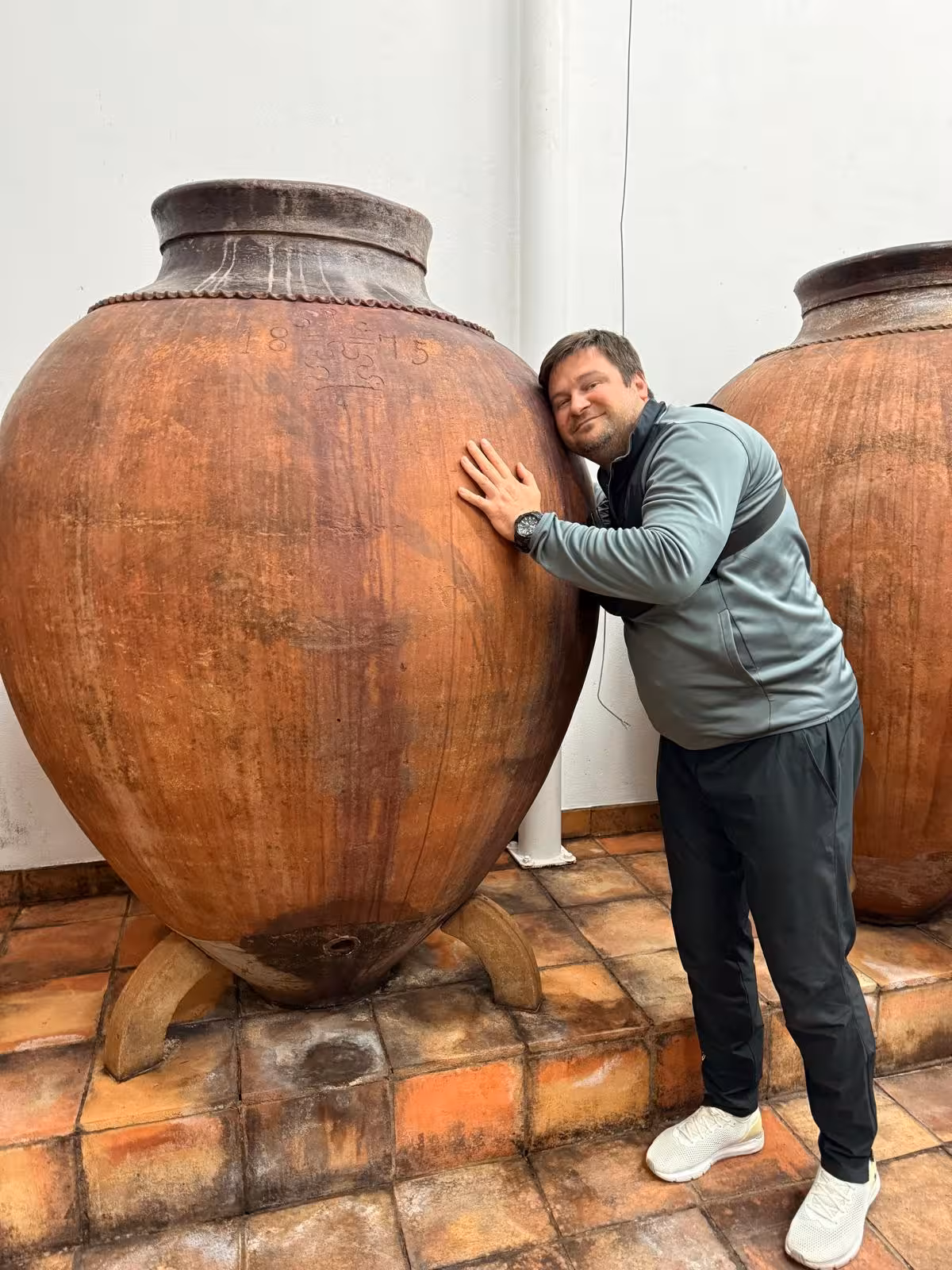 Tourist embracing large clay wine amphorae, experiencing traditional wine-making in Évora, Portugal.
