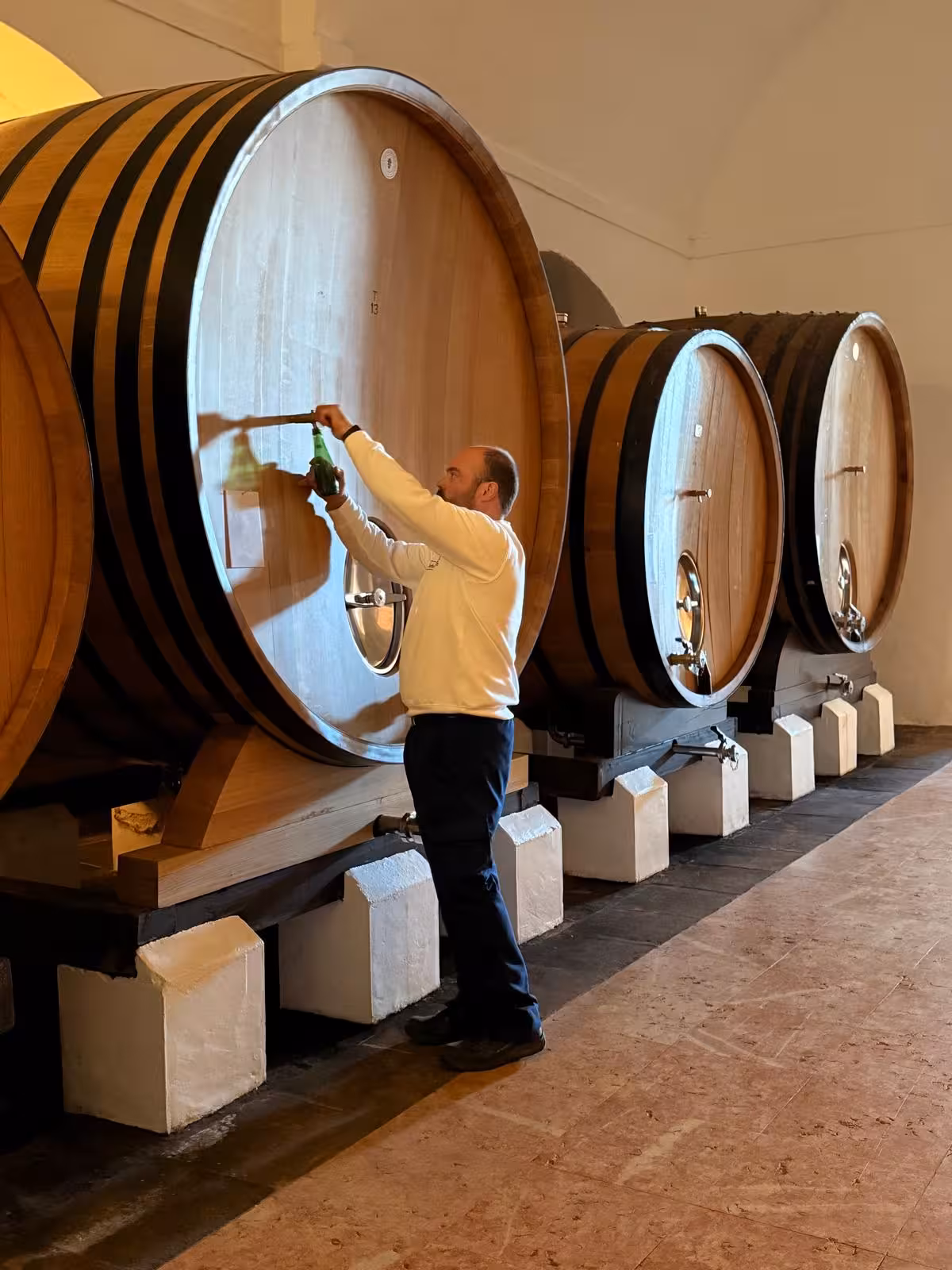 Winemaker samples wine from large oak barrel in historic cellar during Évora's exclusive wine tour.