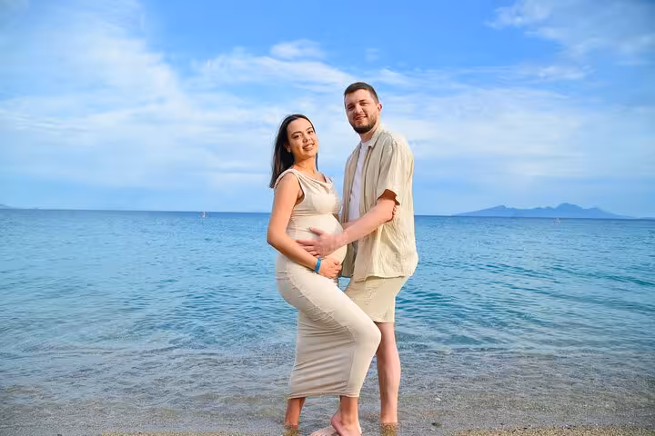 Expecting couple posing on a serene beach in Analipsi, capturing a special moment with stunning sea and sky backdrop.