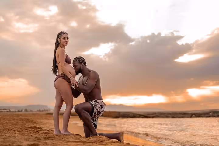 Expecting couple enjoys a tender moment on Gouves beach, set against a beautiful sunset backdrop.