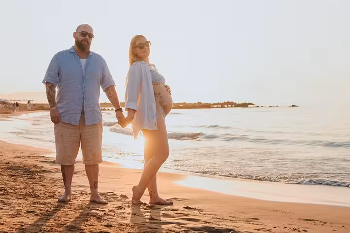 Expecting couple holding hands during a serene sunset beach photoshoot in Gouves, perfect for capturing precious moments.