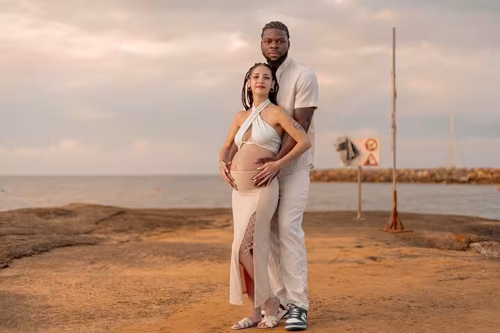 Expecting couple embracing by the sea during sunset, highlighting a serene moment in a Malia photoshoot.
