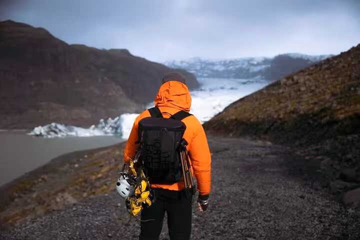 Guide in orange jacket with climbing gear overlooking glacier lagoon on Iceland's south coast