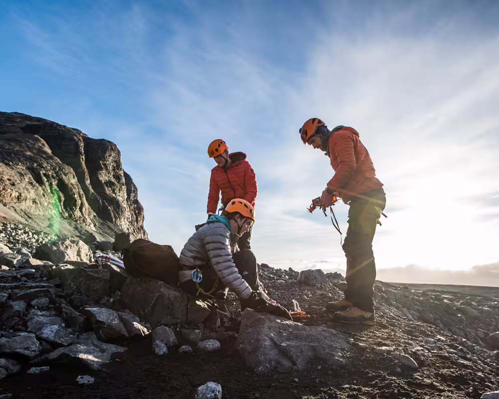 Expert guides and climbers gear up on rocky terrain during a private ice climbing tour on Solheimajokull Glacier