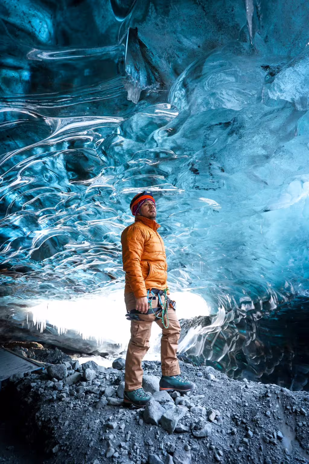 Explorer in orange jacket marveling at glowing blue ice walls inside a private Iceland glacier ice cave tour