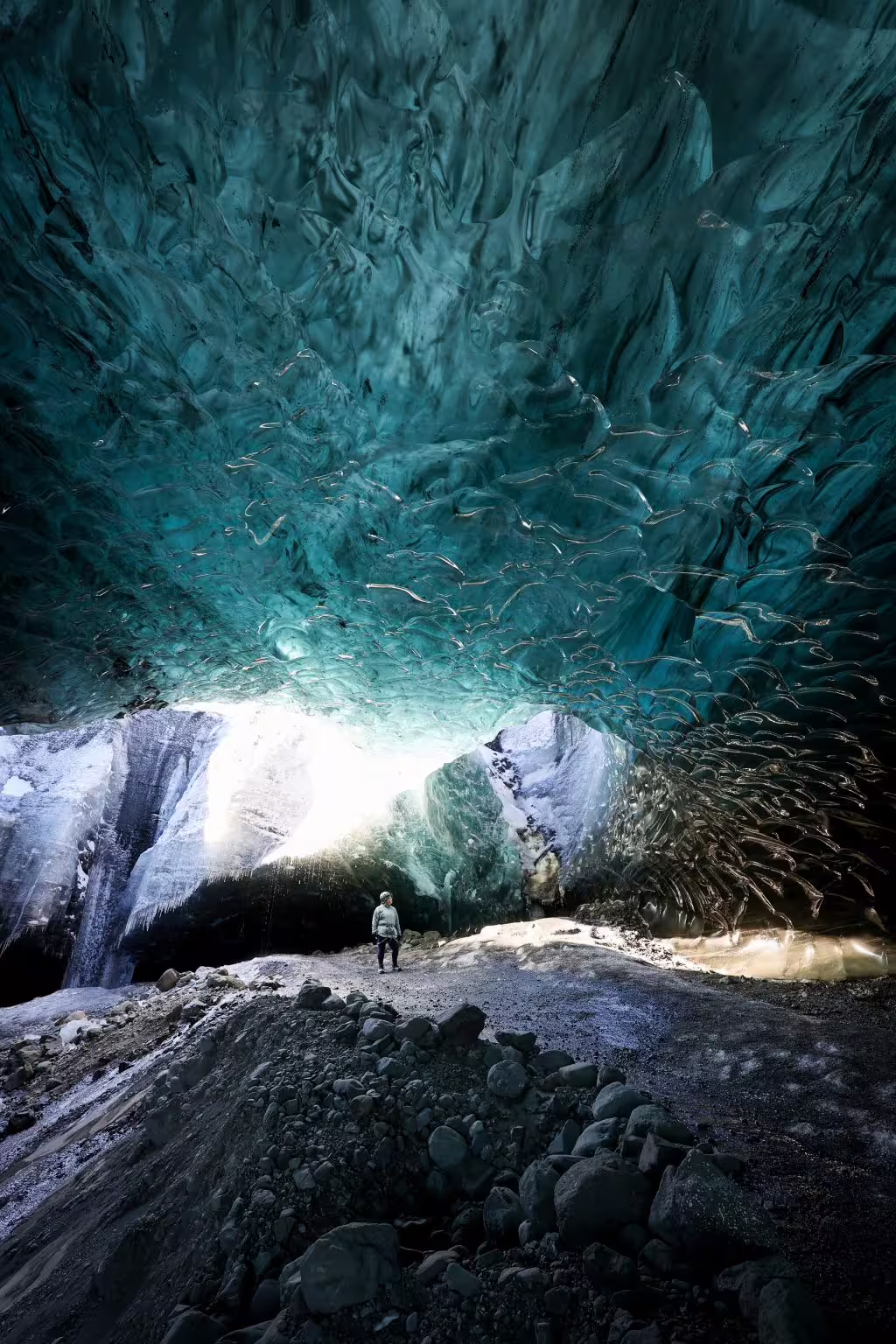 A lone explorer stands beneath a stunning turquoise glacier ice cave ceiling on an Iceland ice cave tour