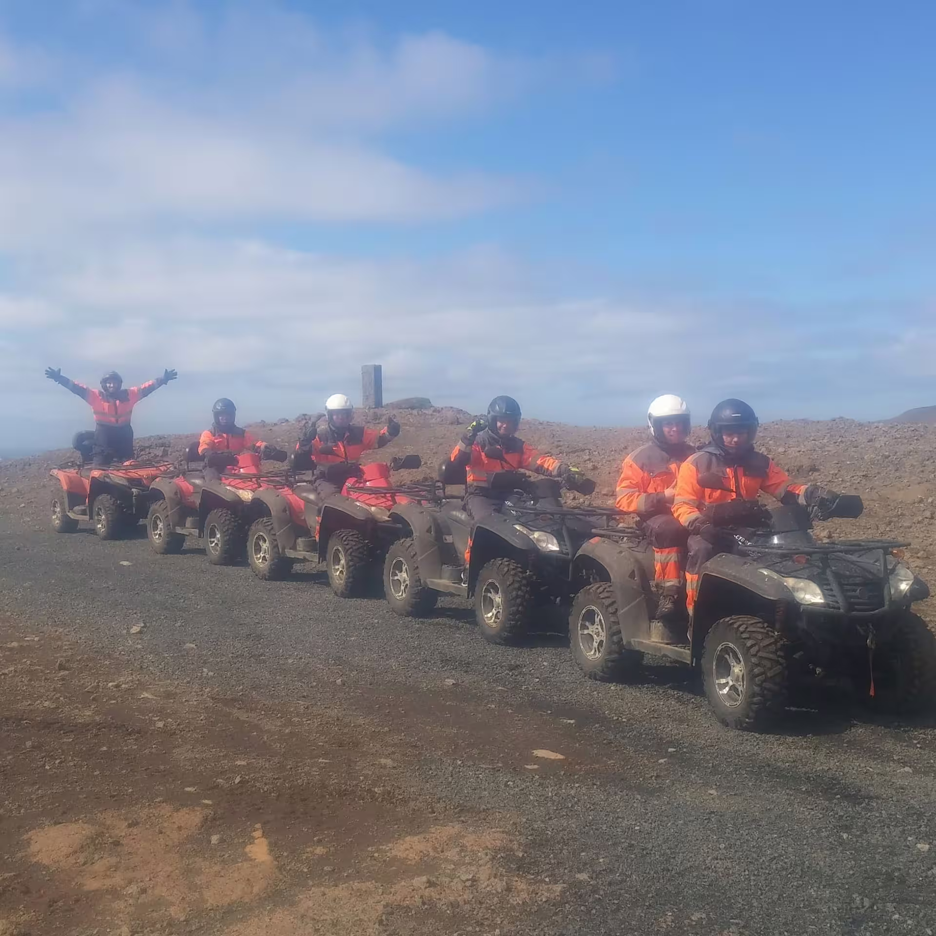 Group of riders in orange gear on ATVs lined up on rocky volcanic terrain in Reykjavik under blue sky