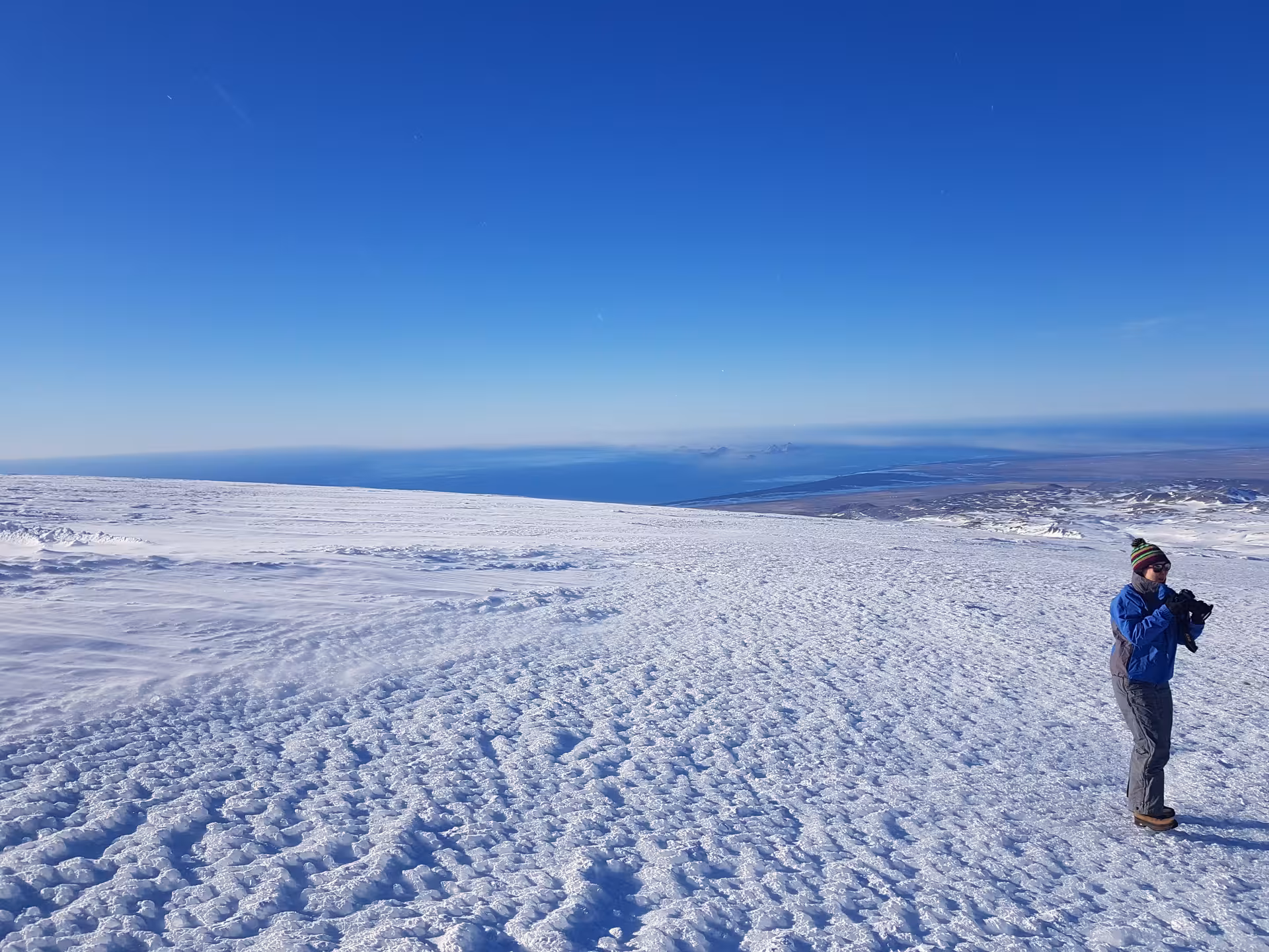 Hiker photographing vast snowy Eyjafjallajokull glacier summit with blue ocean view in Iceland