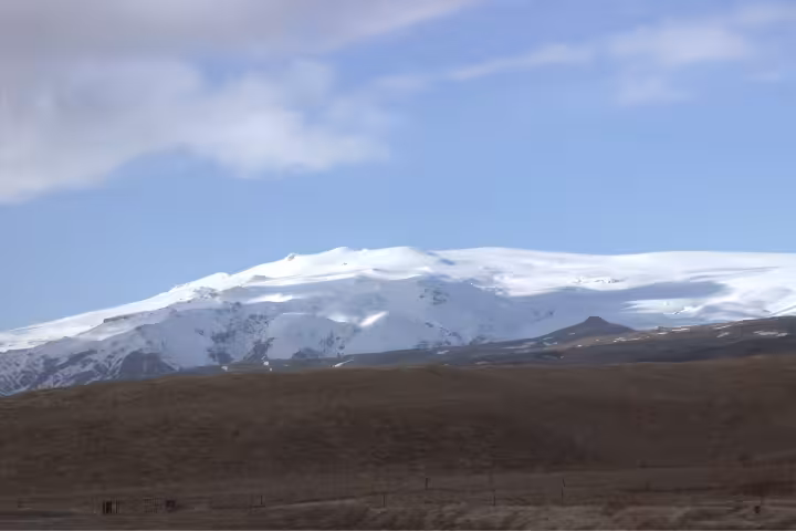 Snow-capped Eyjafjallajokull glacier summit rising above brown Icelandic plains under blue sky