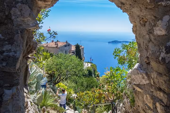 Stone arch framing lush gardens and Mediterranean sea view in Eze village, French Riviera