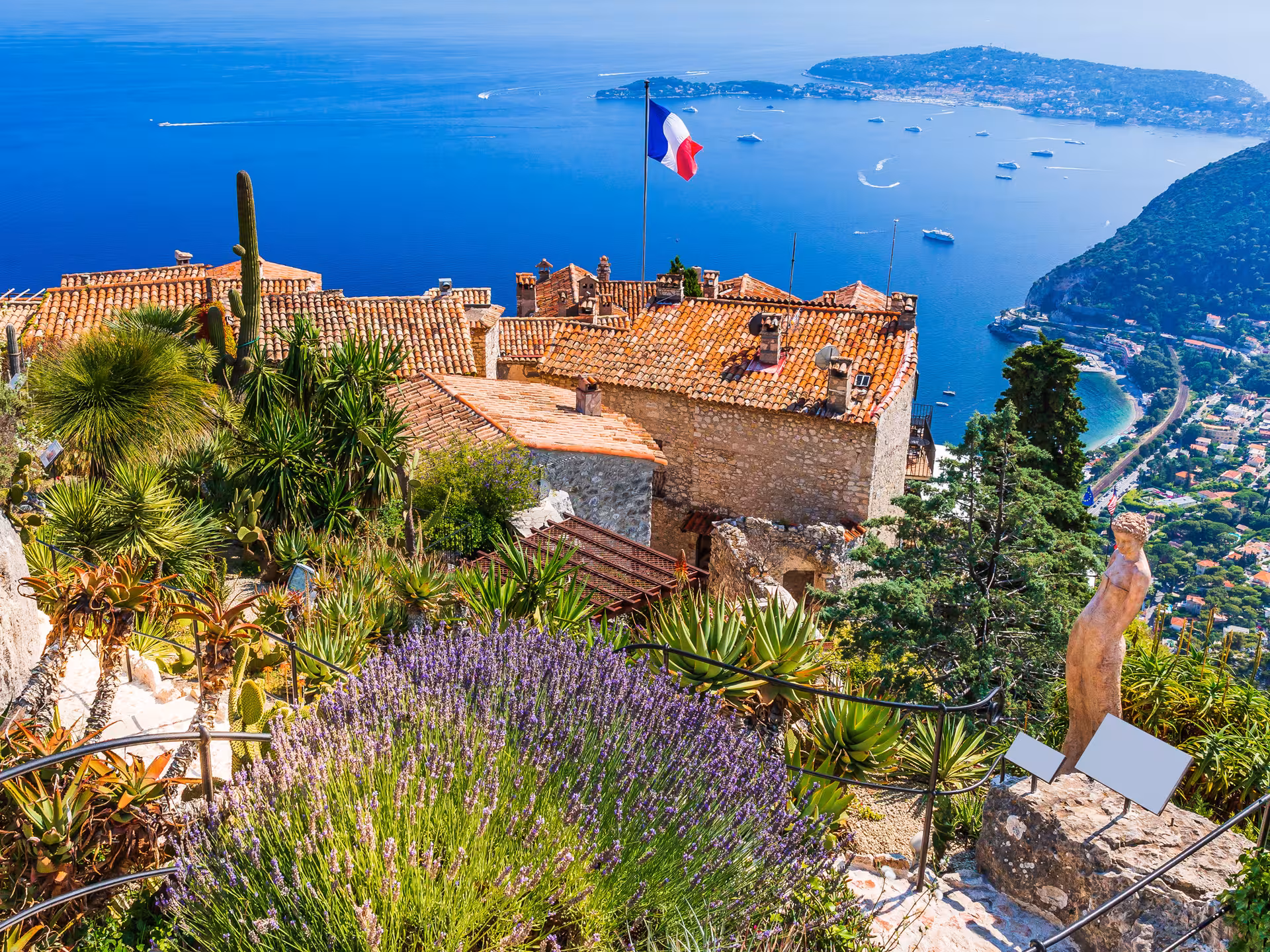 Panoramic view of Eze Village perched on hilltop with French flag, exotic gardens, and Mediterranean Sea coastline