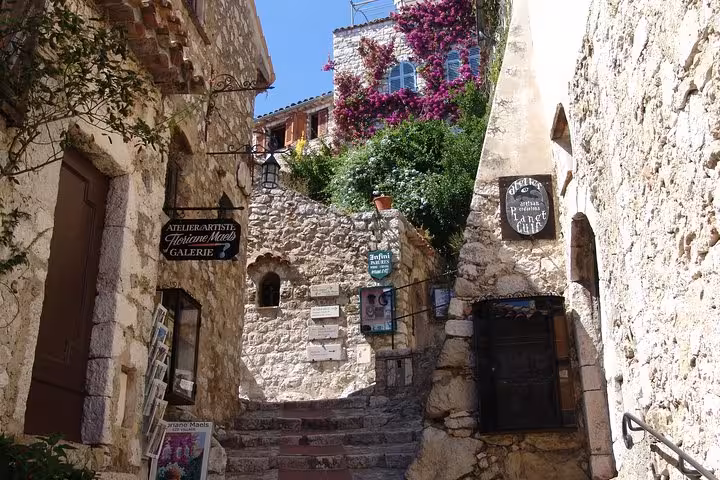 Narrow stone alleyway with art gallery signs and bougainvillea flowers in Eze Village, France