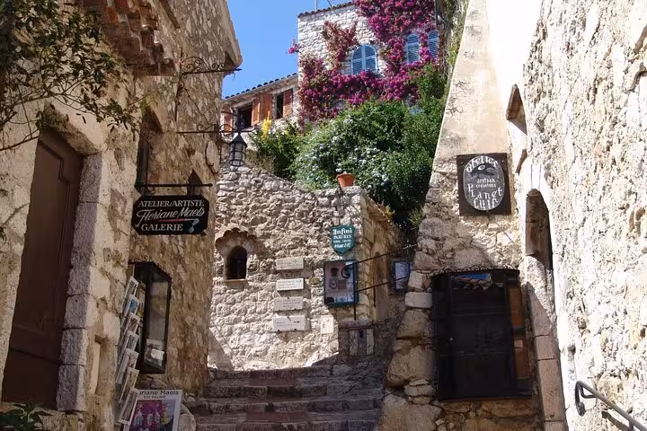 Charming stone pathway in Eze village lined with shops and vibrant flowers, perfect for exploring on a private tour.