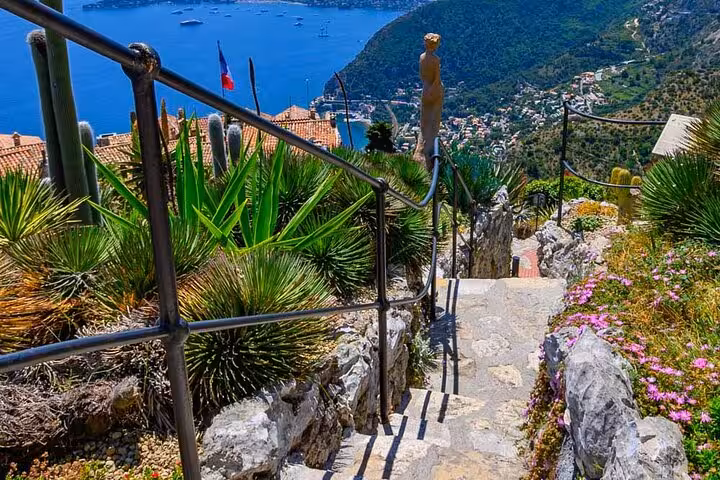 Stone stairway with iron railings overlooking Eze village and Mediterranean Sea with French flag visible