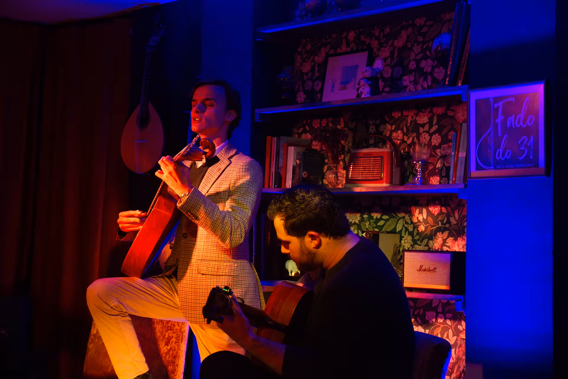 Two musicians passionately perform Fado music in an intimate, dimly lit setting, featuring traditional guitars.