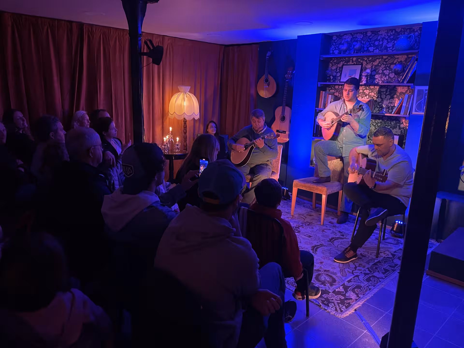 Intimate Fado performance with guitarists captivating an engaged audience in a cozy, candlelit venue.
