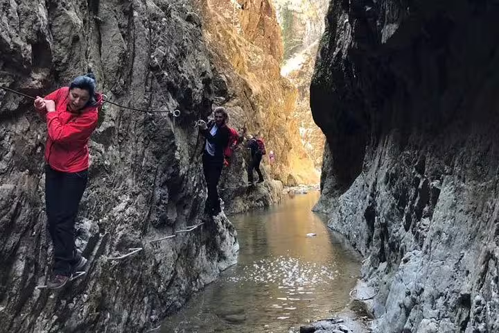 Hikers traversing narrow canyon walls on rope cables above a mountain stream in Fagaras
